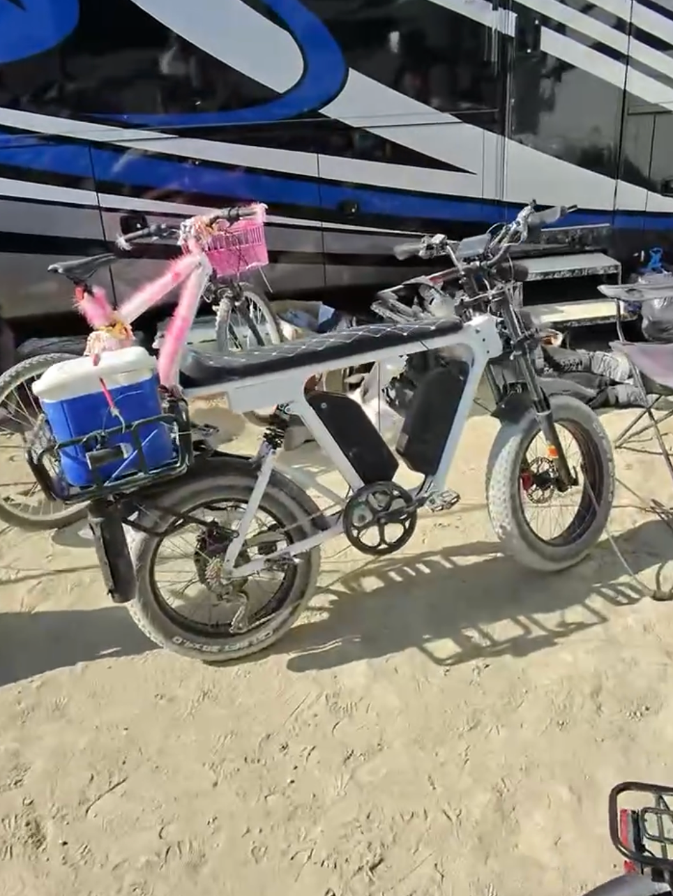 White DUST eBike loaded with a cooler and Hot Pink fur, parked in the sand
