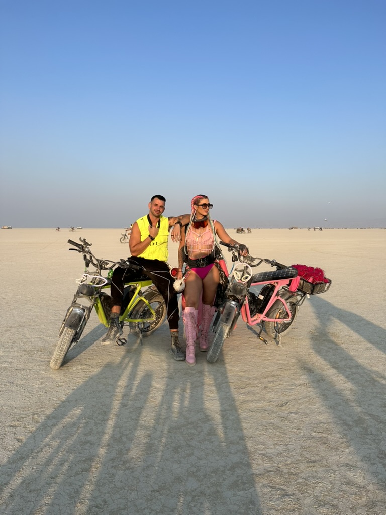 Two DUST riders on neon green and Hot Pink eBikes on the open playa